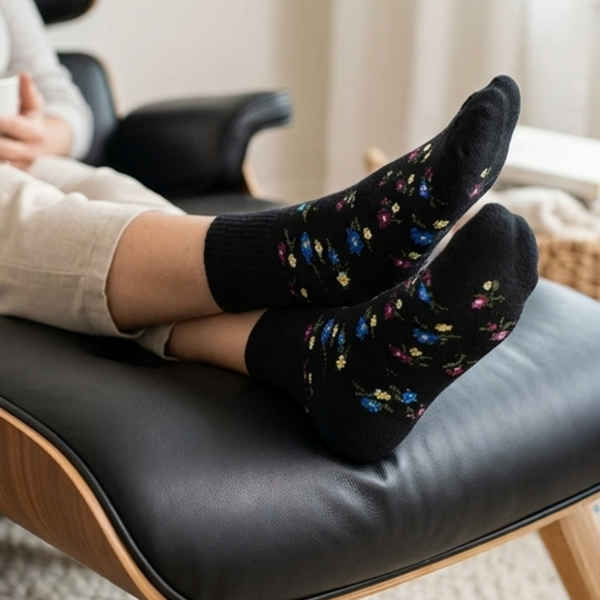 Person wearing black socks with colorful patterns sitting on a chair.